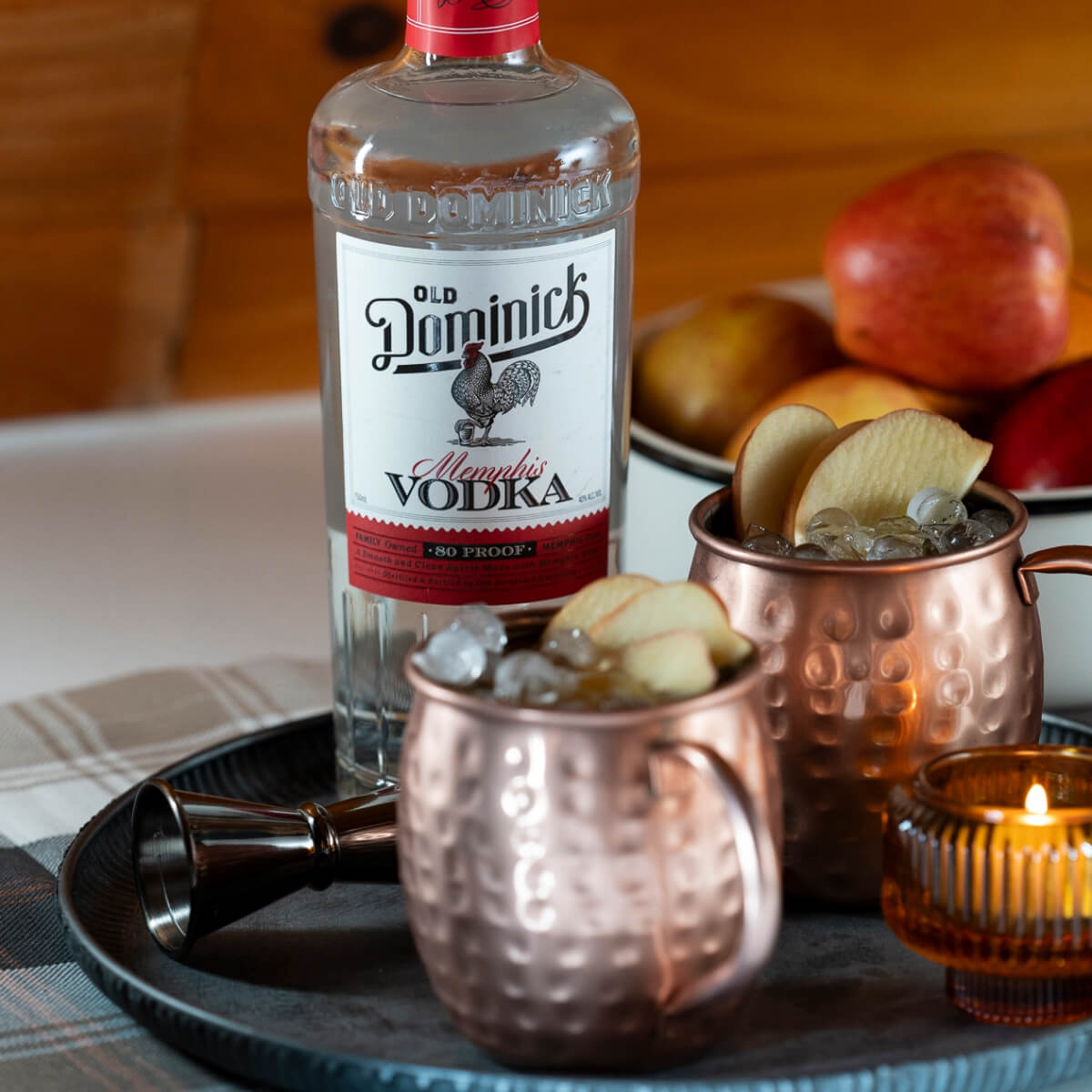 Bottle of Memphis Vodka sitting on a platter with two apple cider Moscow Mules in copper mugs