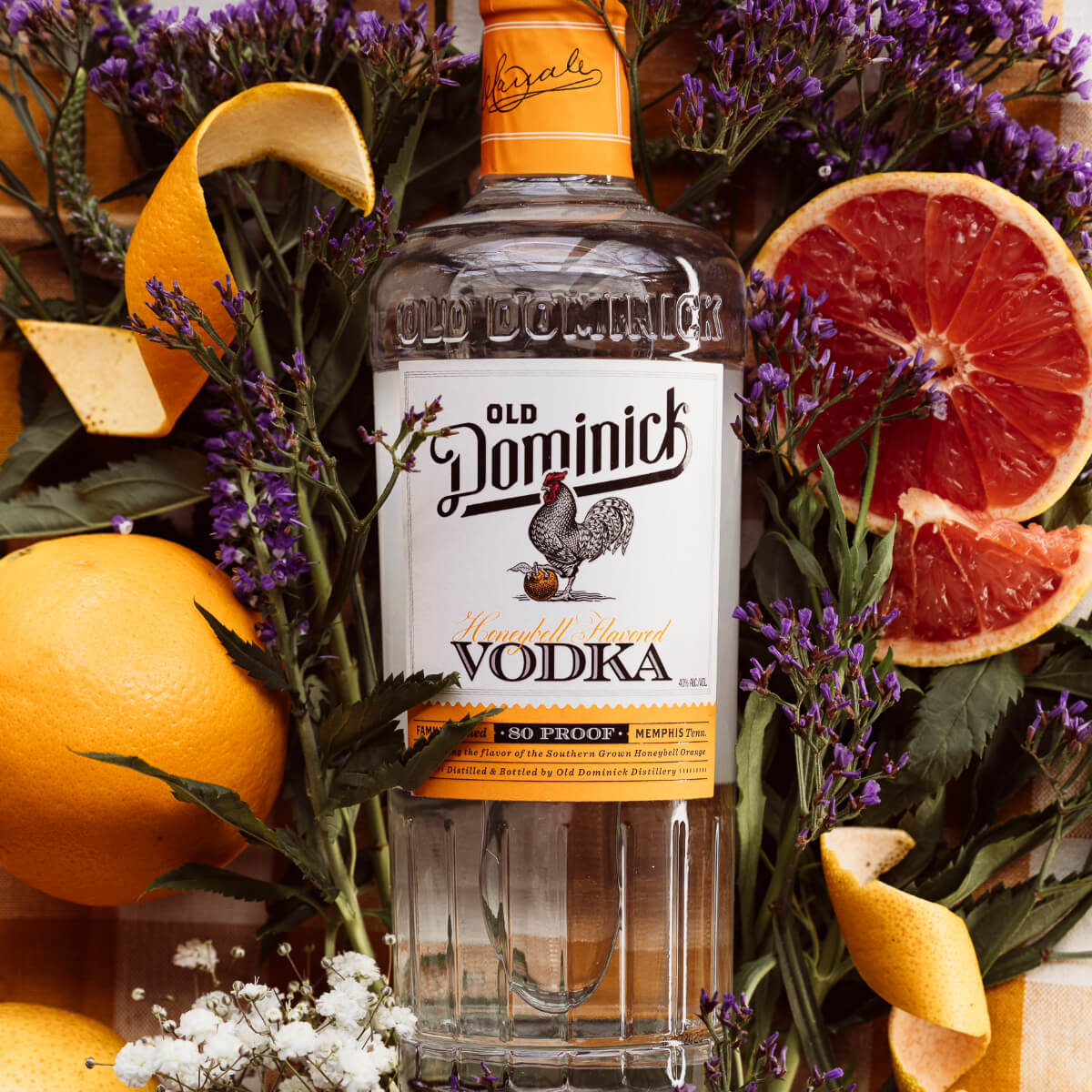 Bottle of Honeybell Citrus Vodka laying in a bed of fresh lavender, surrounded by sliced citrus